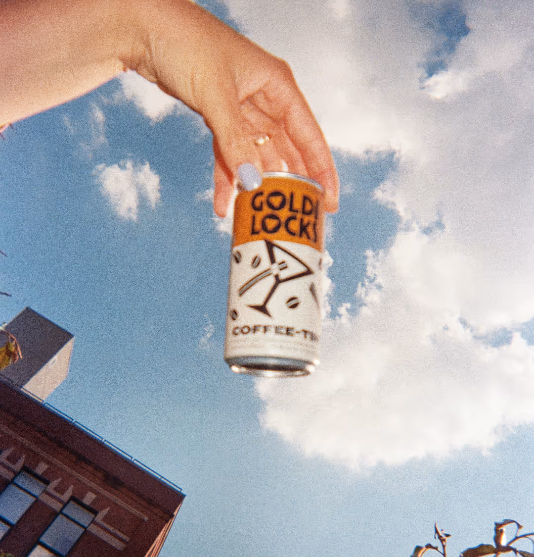 A hand holds a Goldi Locks can, blue skies behind it.