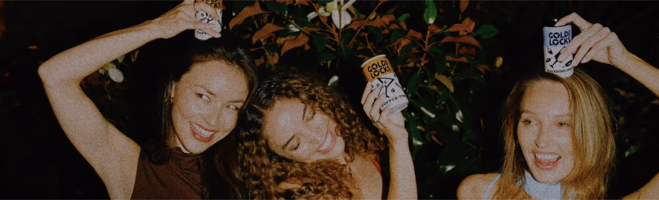 A group of ladies happily hold cans of Goldi Locks, they seem to be at a party of sorts.