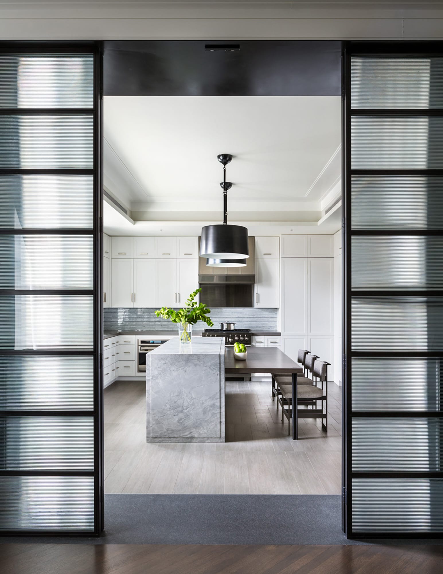 Contemporary kitchen with marble island and pendant lights.