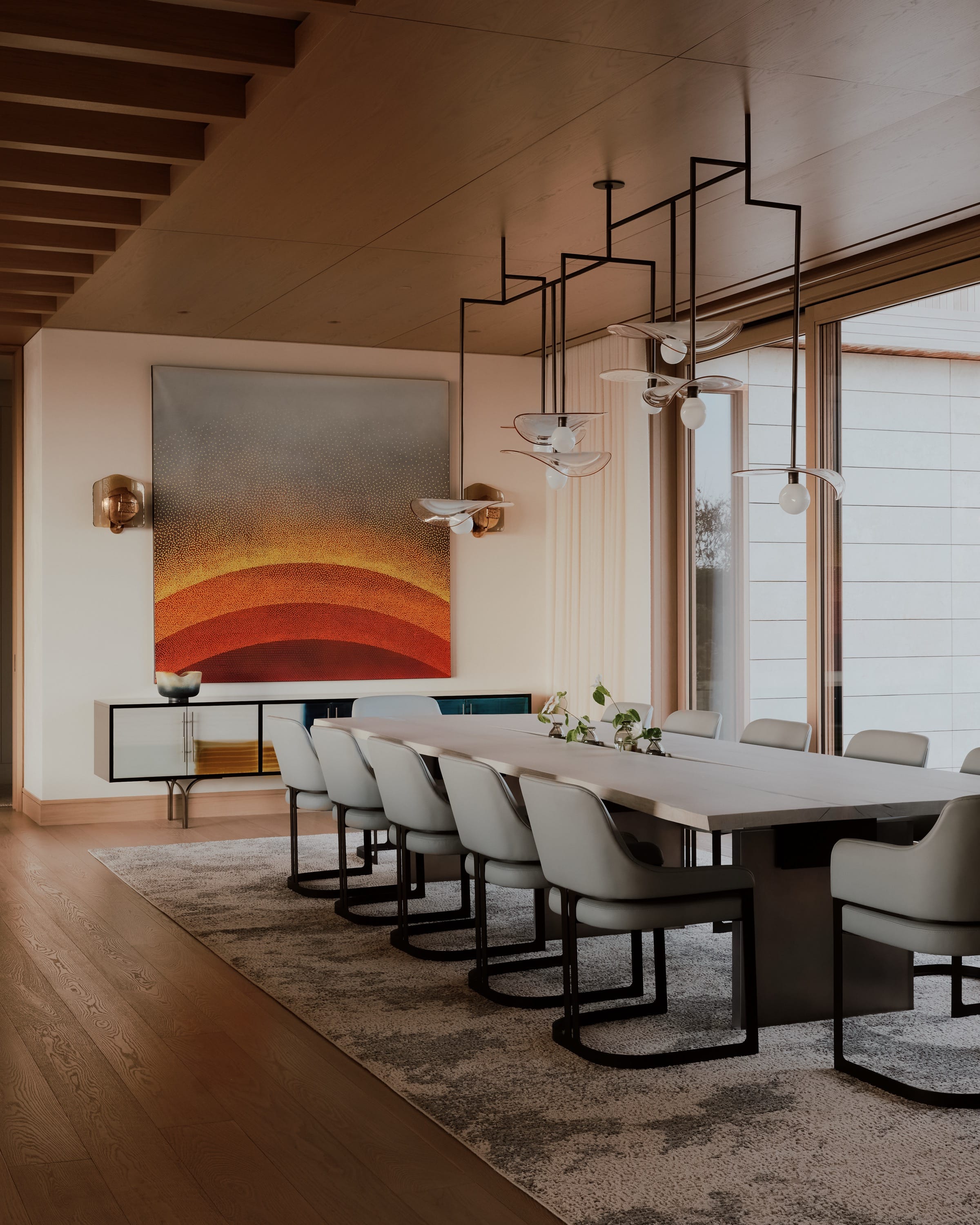 Dining room with long table, pendant lights, and abstract art.
