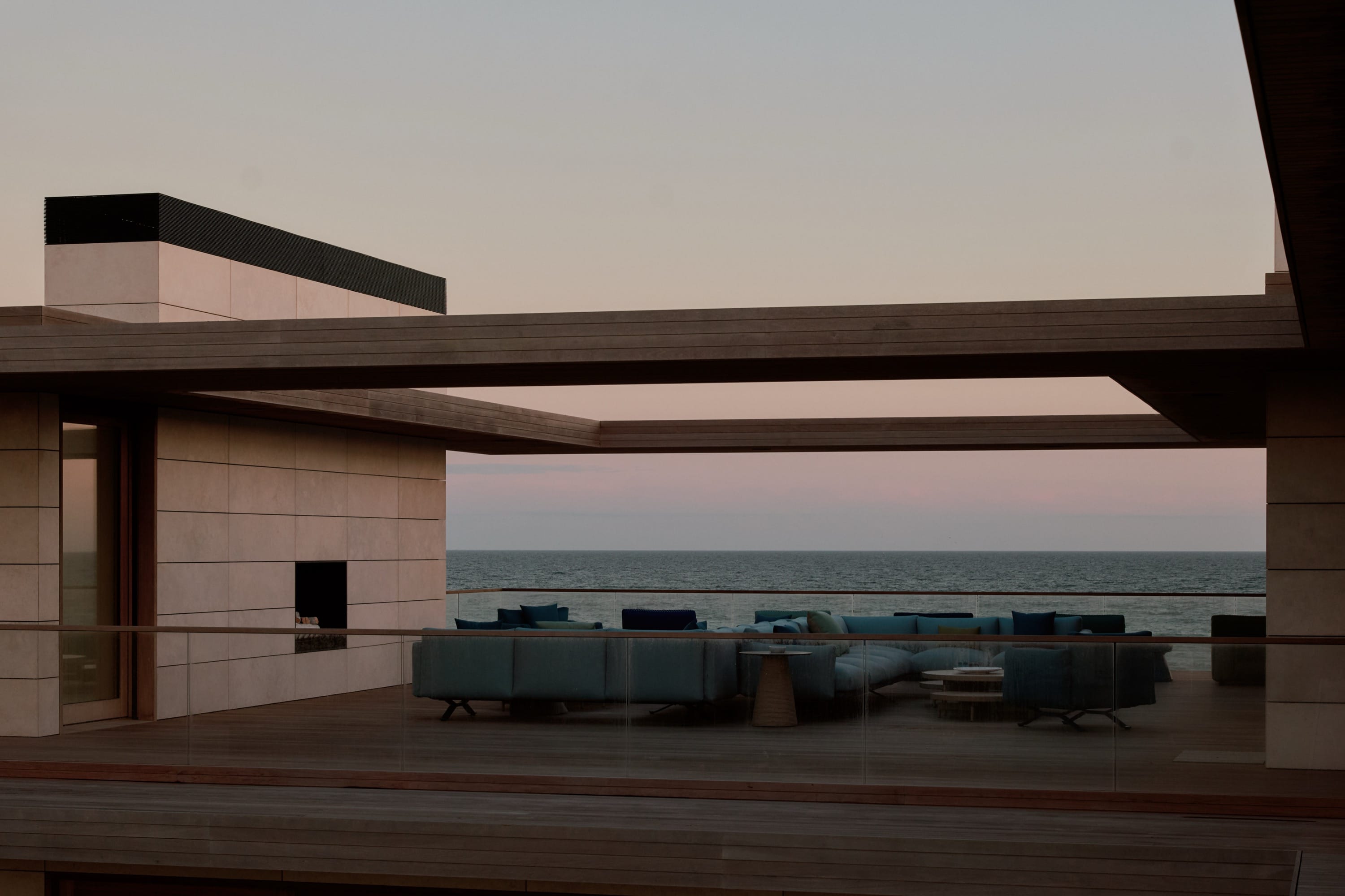 Covered outdoor lounge with sectional and ocean backdrop.