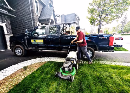 Male worker mowing lawn in front of a black truck