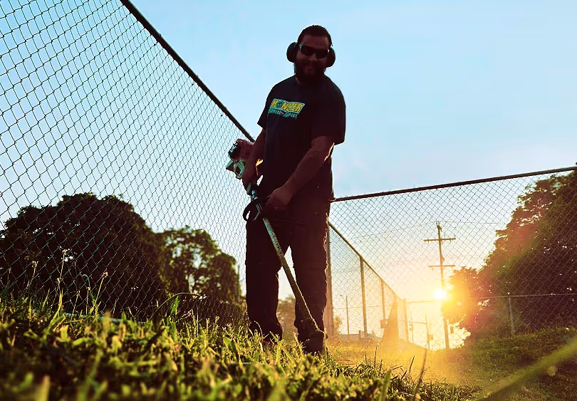 trimming grass along a fence line at dusk