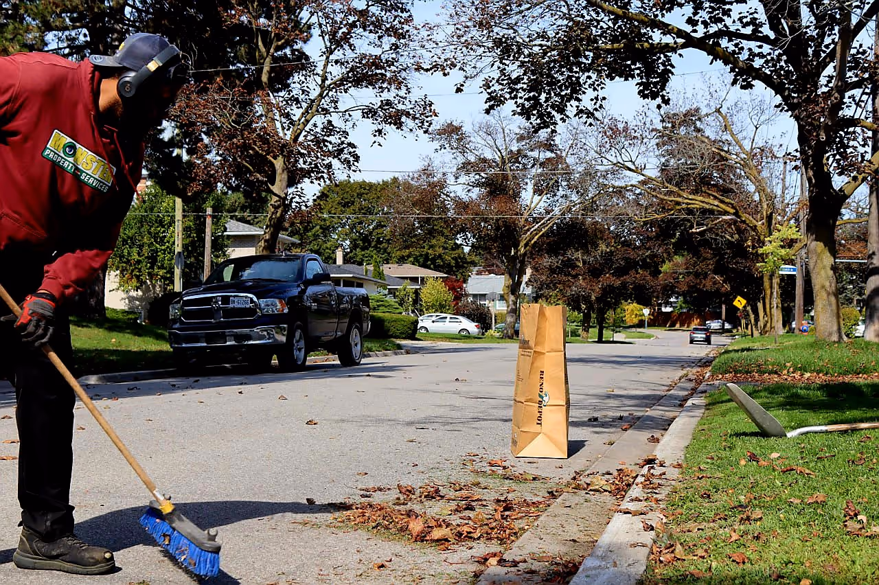 Monster crew member sweeping leaves at the curb of a residential street in Toronto during a fall cleanup visit