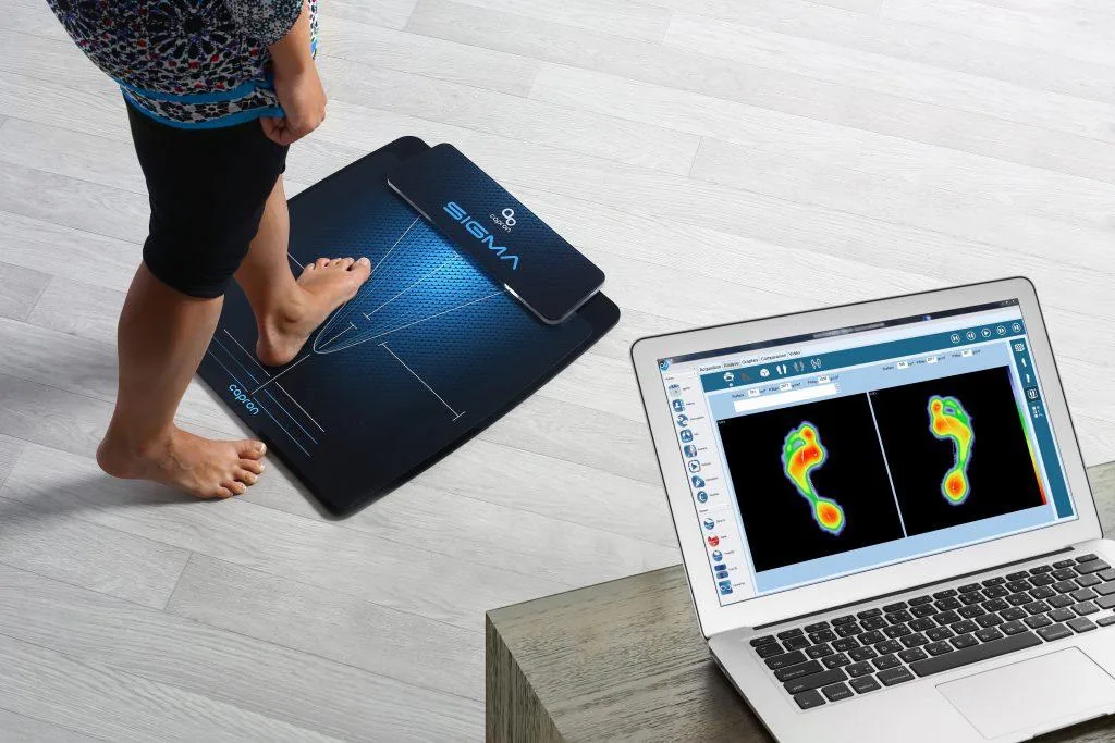 Badanie na platformie pedobarograficznej z mapą nacisku stóp na ekranie laptopa