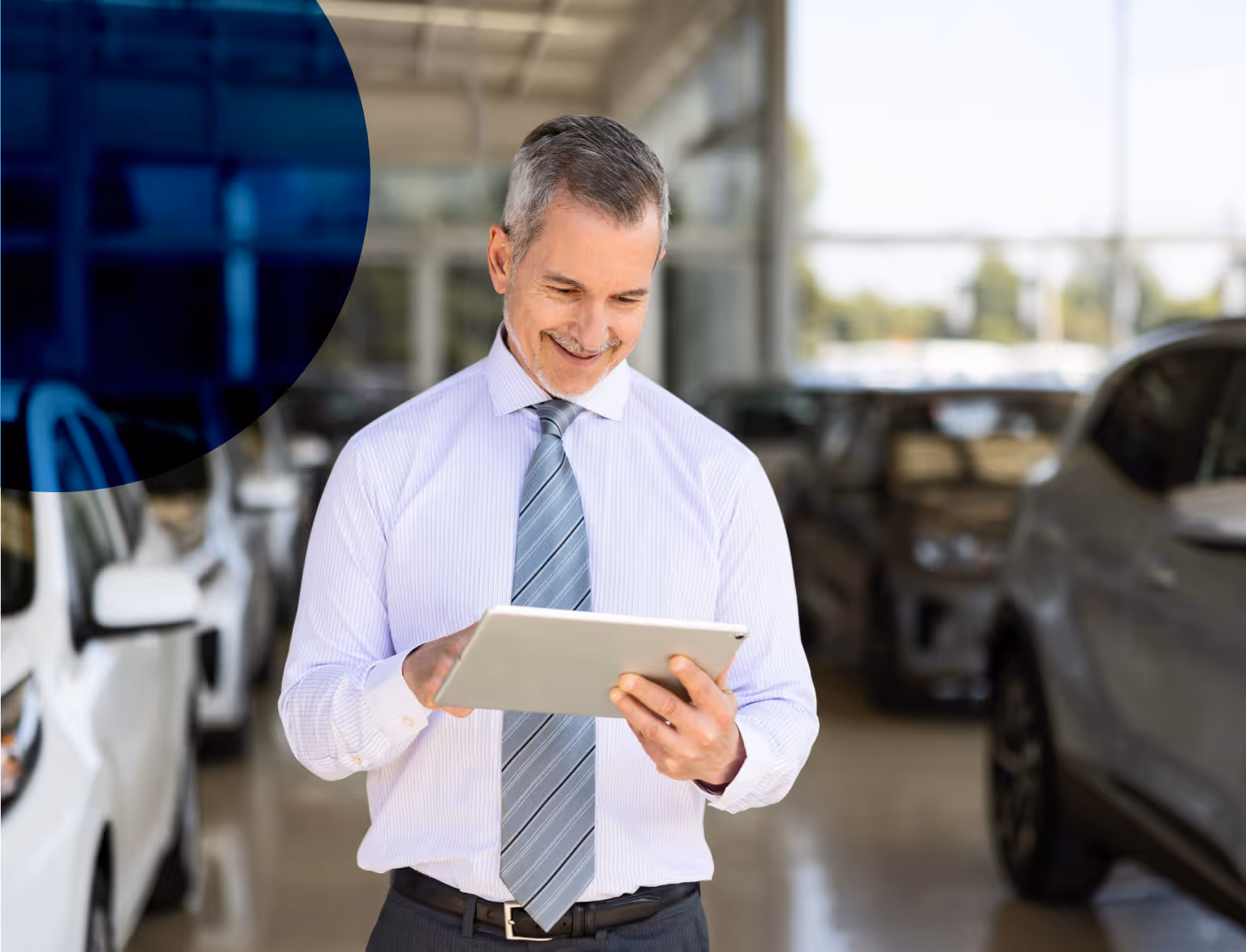 man looking down on an ipad, he stands in a car dealership