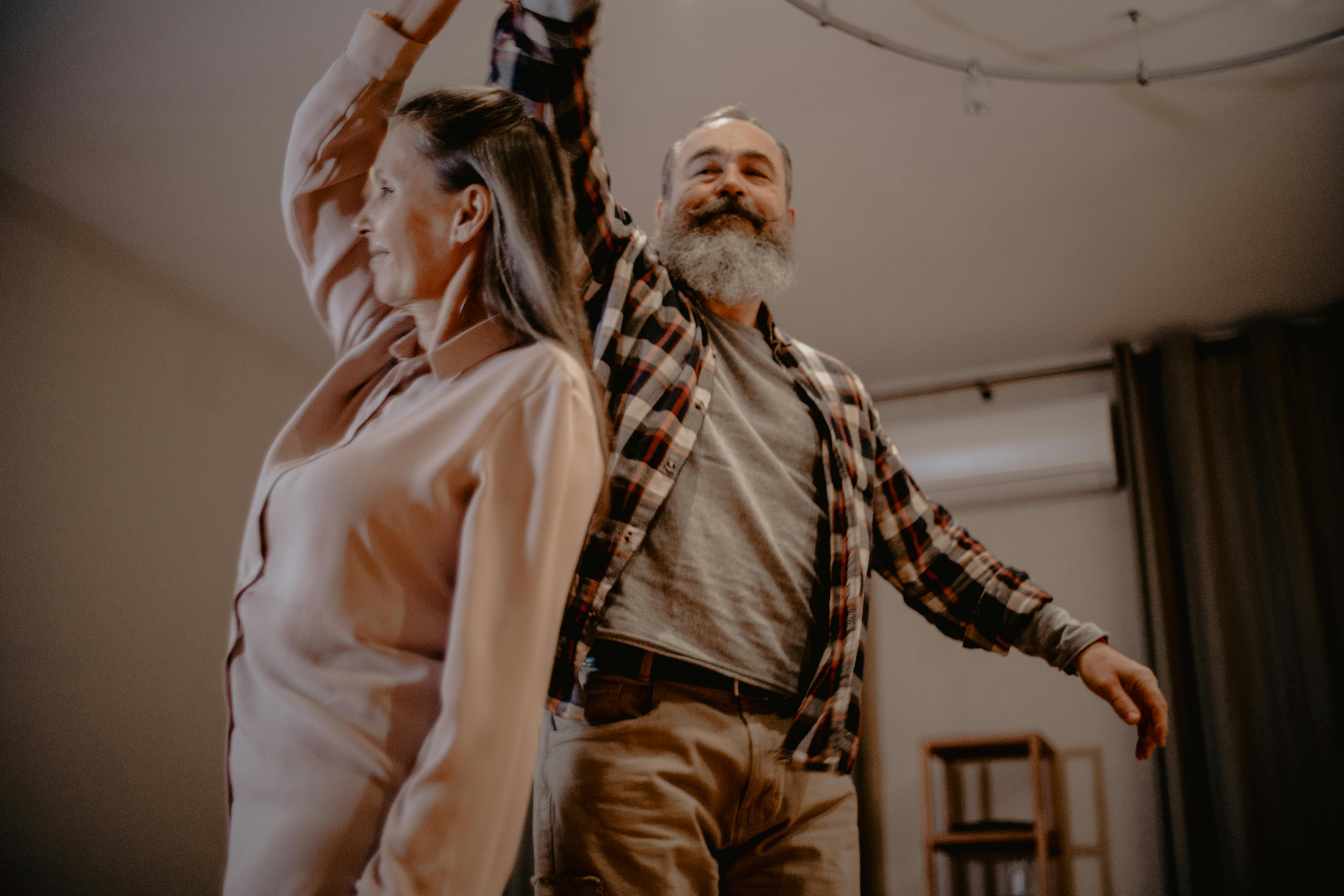 Smiling older couple dancing together at home, with the man twirling the woman in a warm, relaxed setting, capturing joy and active senior living.