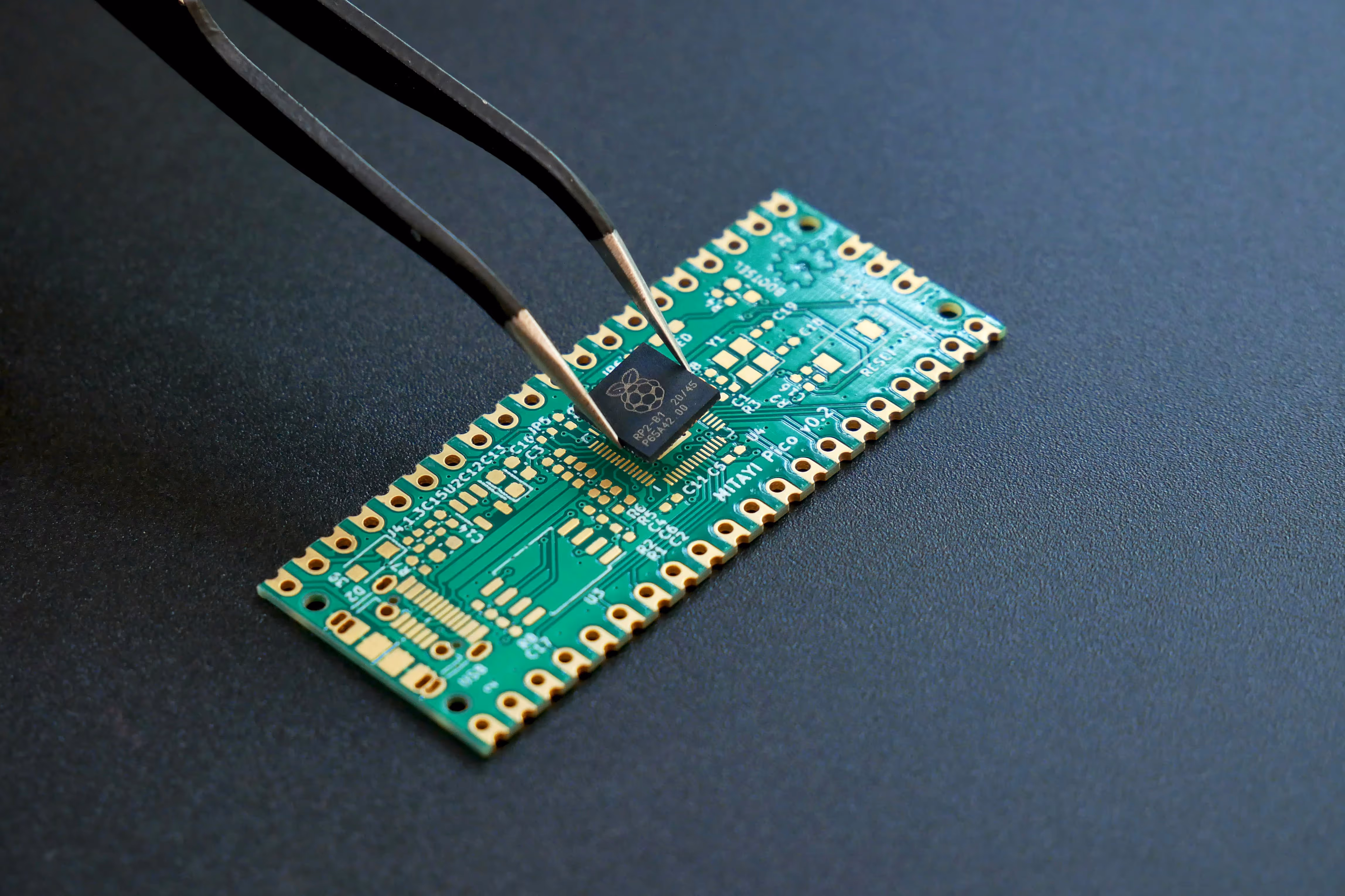 Electronic tweezers holding a Raspberry Pi Pico microcontroller chip above a green circuit board.