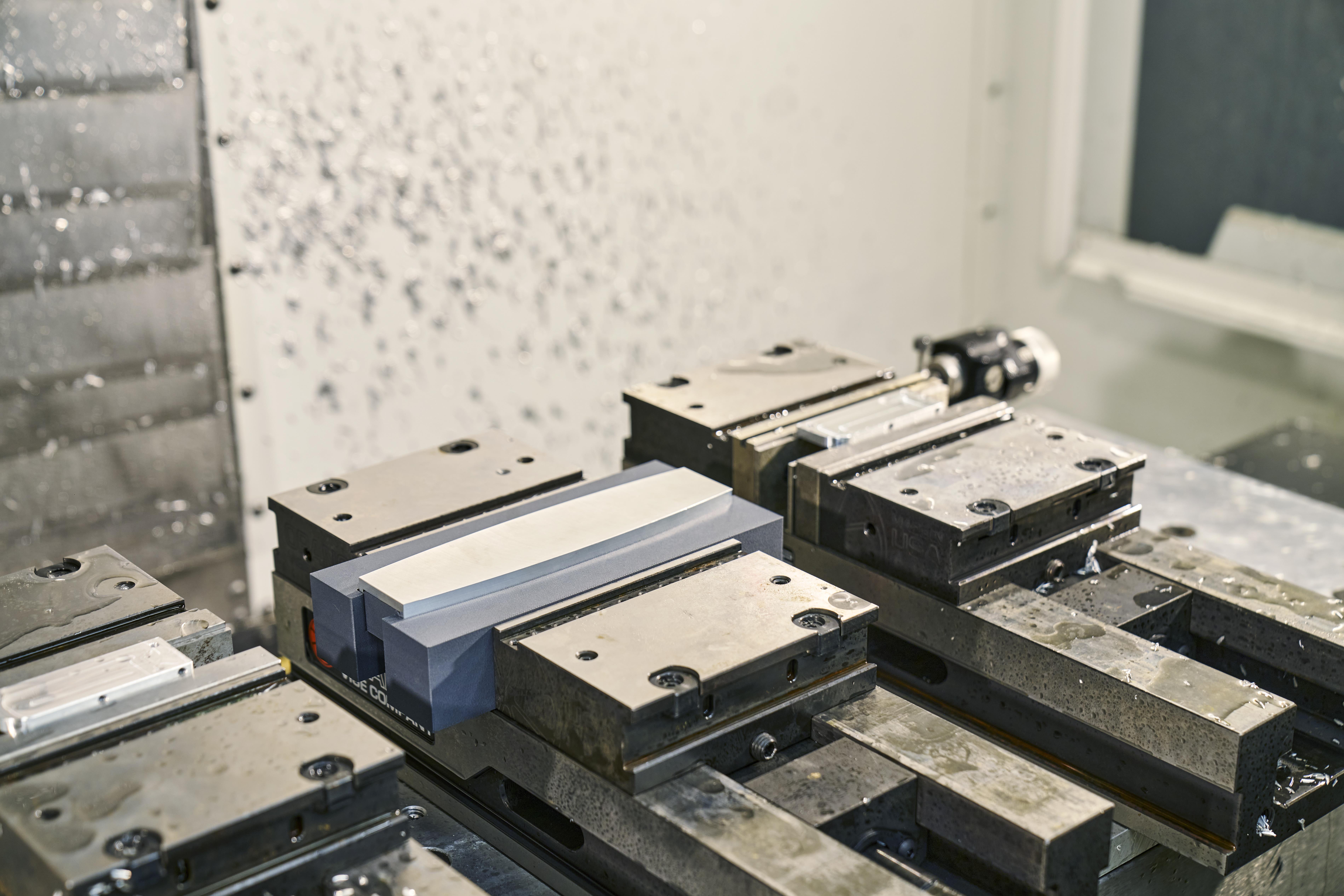 Metal block secured in a CNC machine vise ready for precision milling.