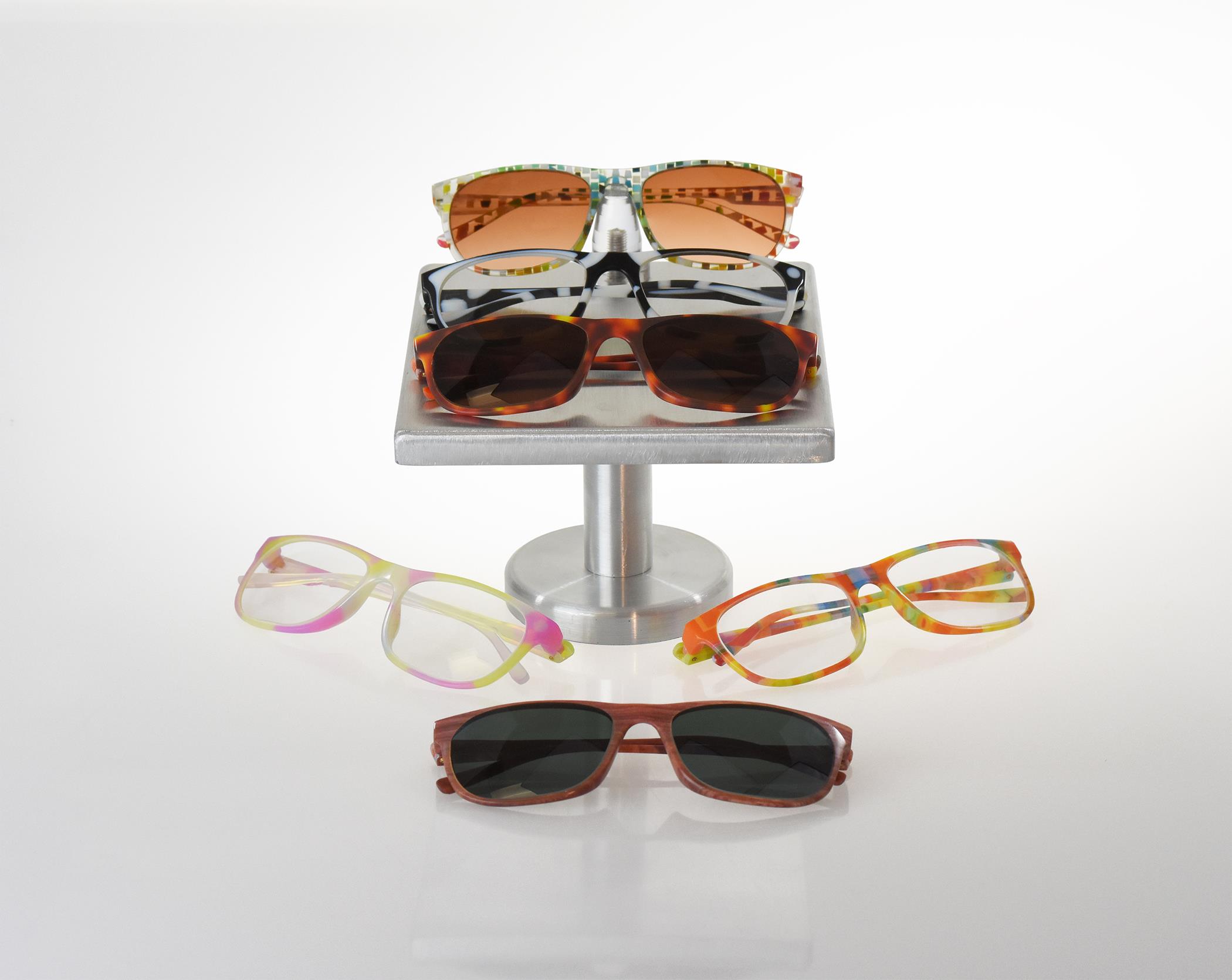 Assortment of six colorful eyeglasses and sunglasses displayed on a small metal stand and white surface.