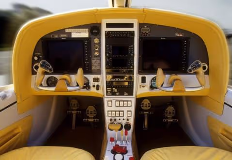 Cockpit of a small aircraft with dual control yokes, digital screens, and yellow seats.