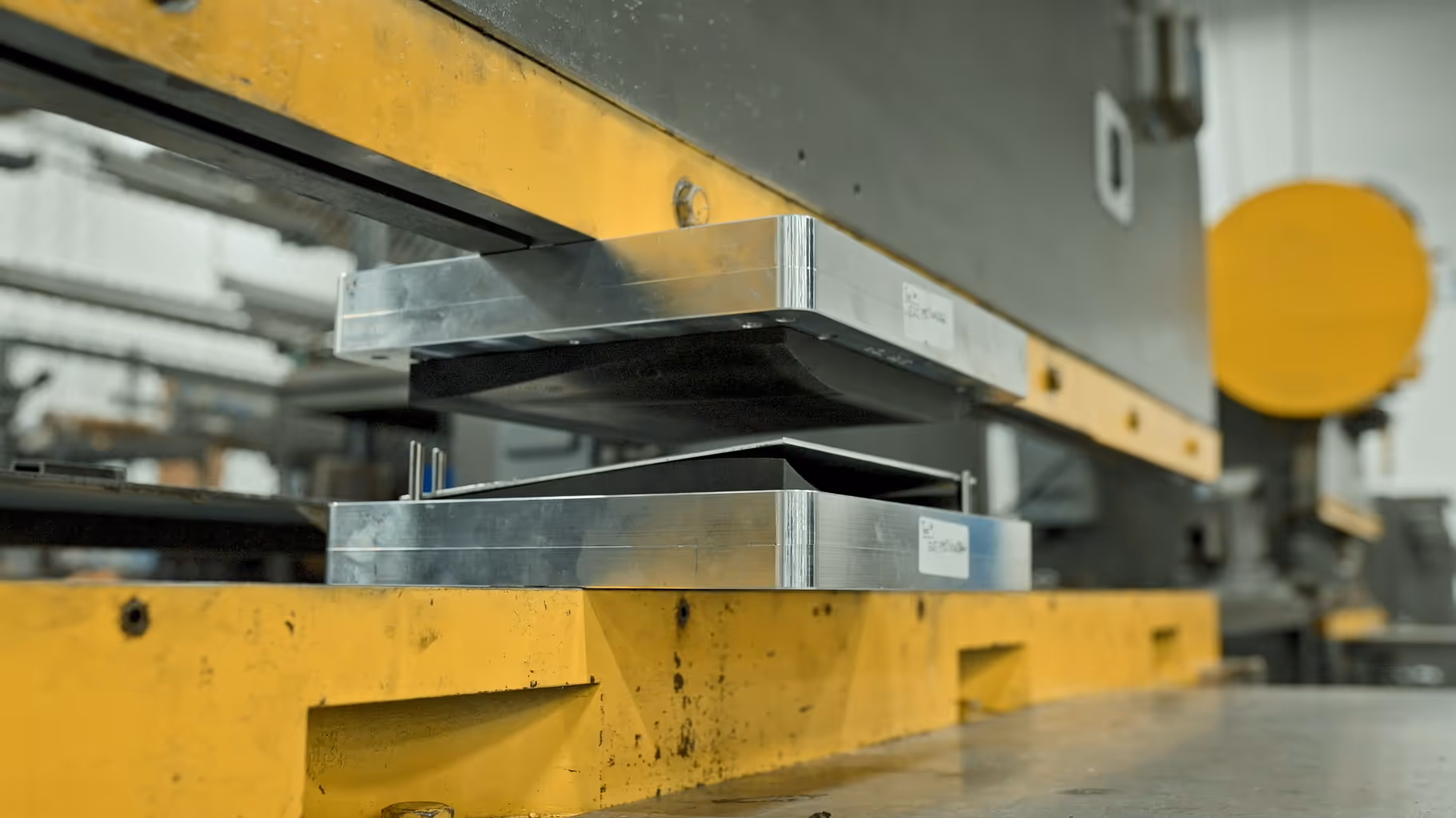 Close-up of a metal forming die press with upper and lower steel plates in an industrial workshop.