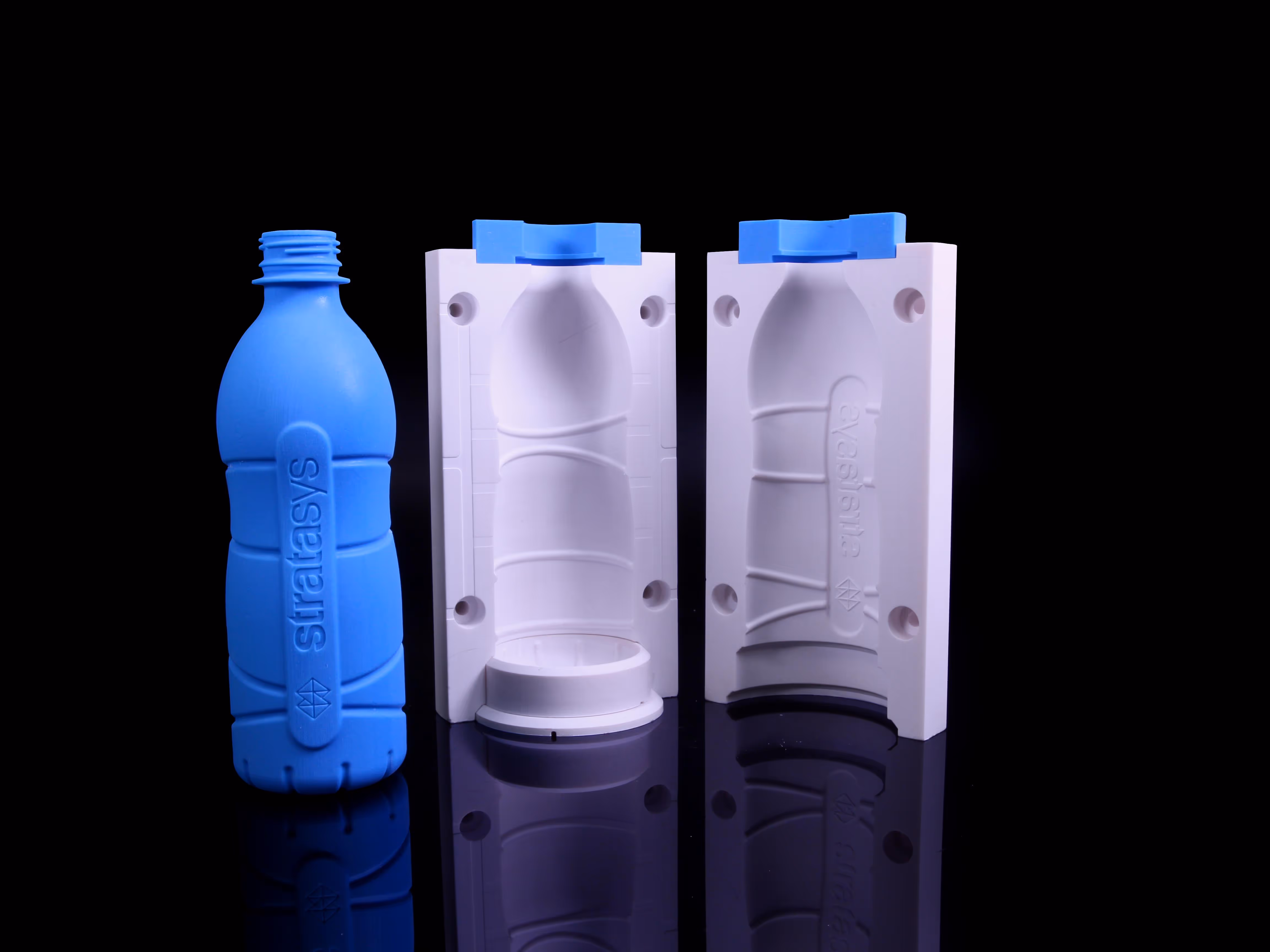 Blue 3D printed bottle prototype with 'Stratasys' text next to two white plastic mold halves shaped for the same bottle on a reflective surface.
