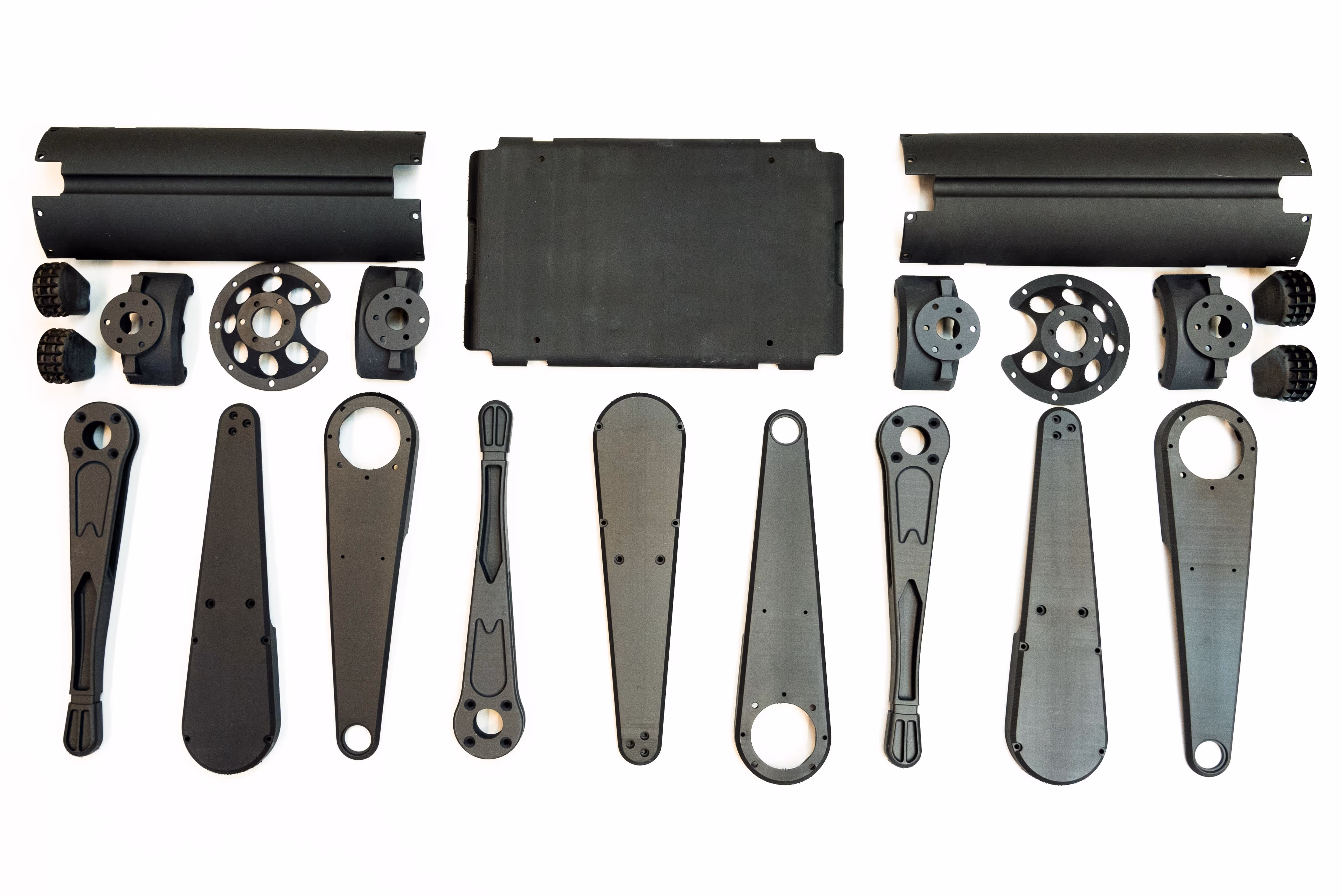 Assorted black mechanical parts and components arranged on a white surface.
