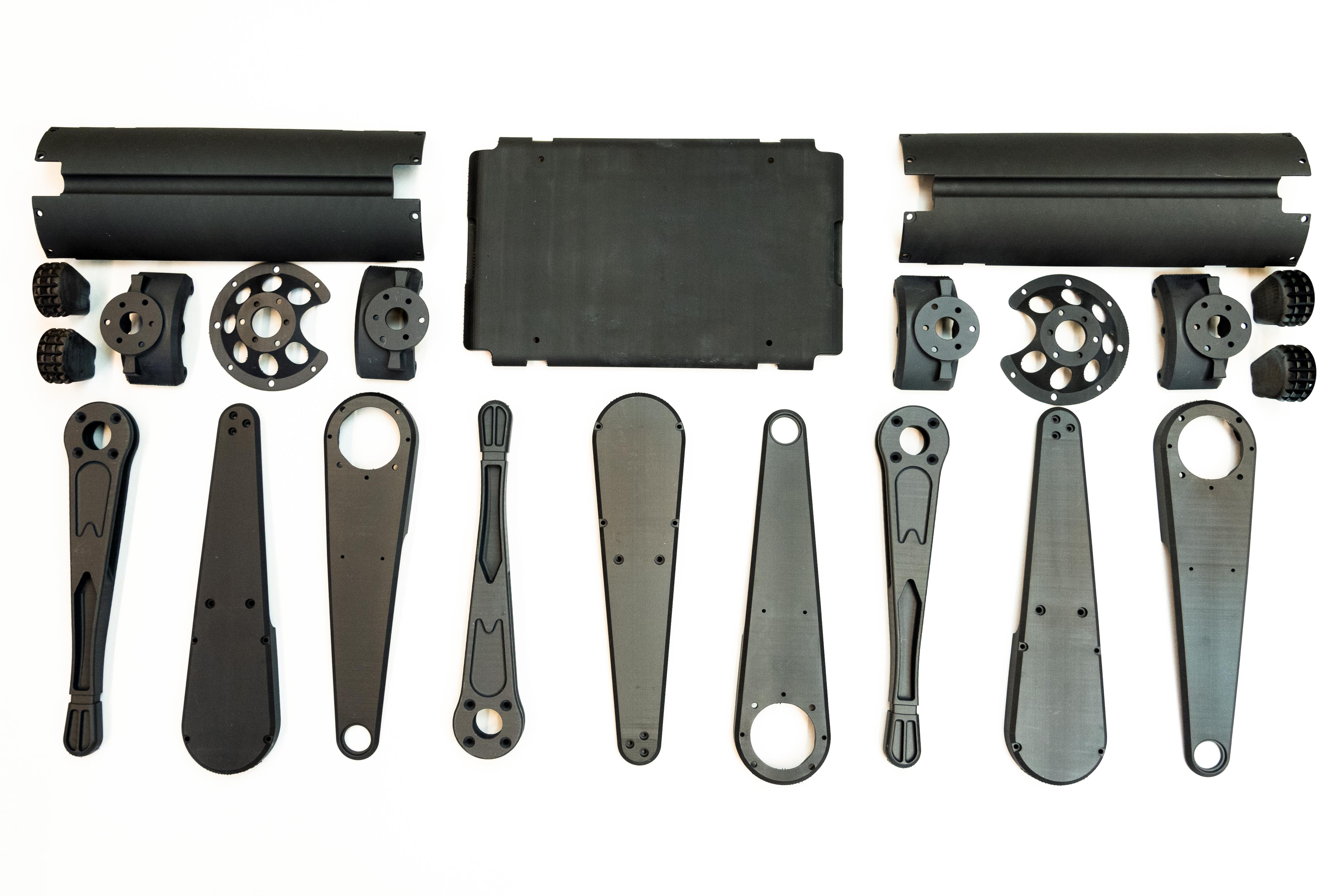 Assorted black mechanical parts and components arranged on a white surface.