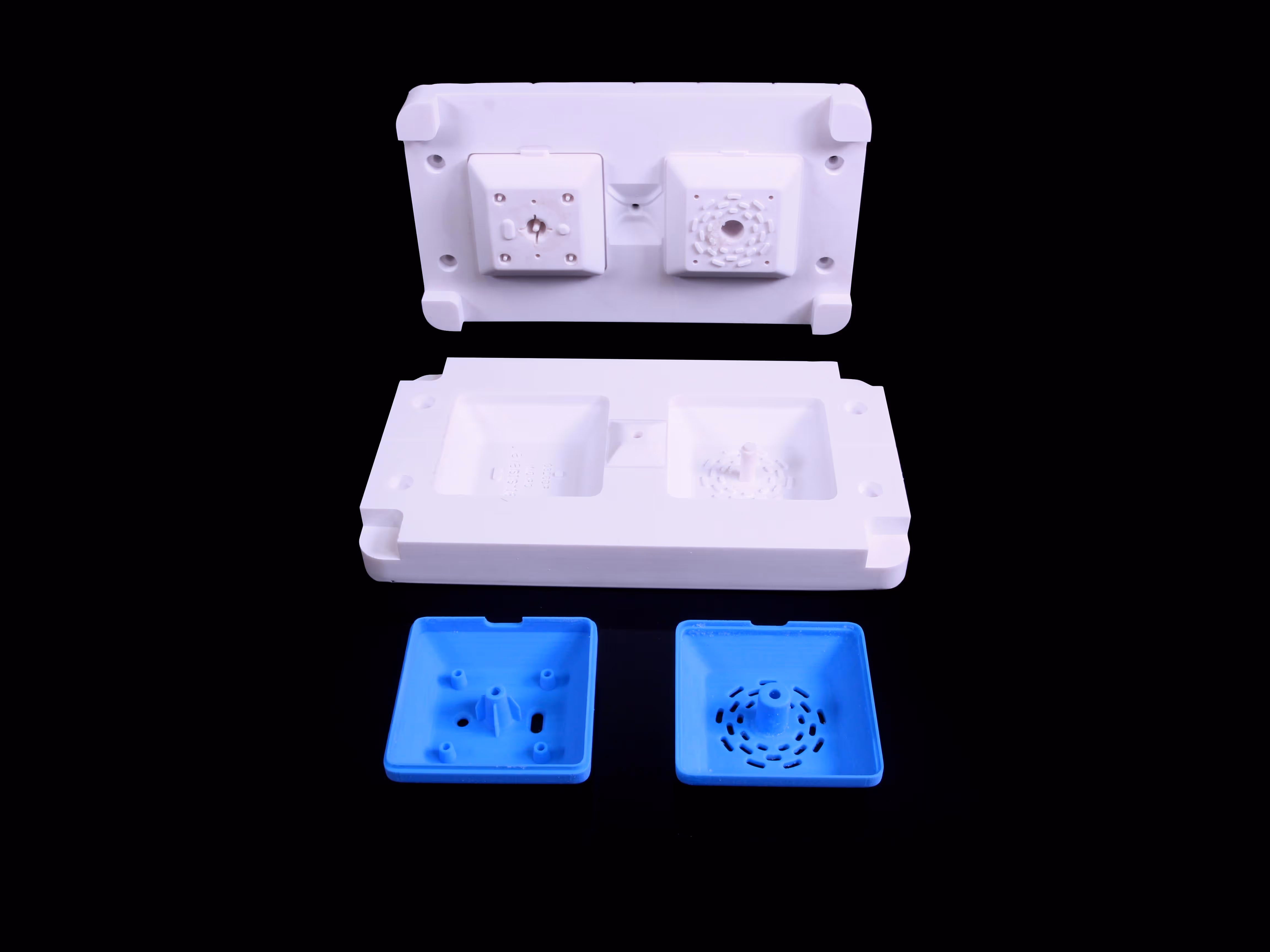 White injection mold parts displayed above two blue plastic molded components on a black background.