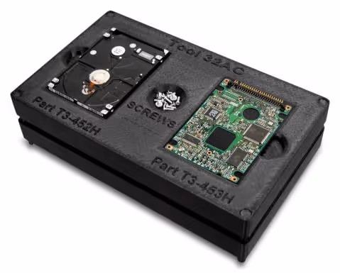 Black hard drive fixture tool with labeled slots holding a hard drive platters assembly, screws, and a green circuit board.