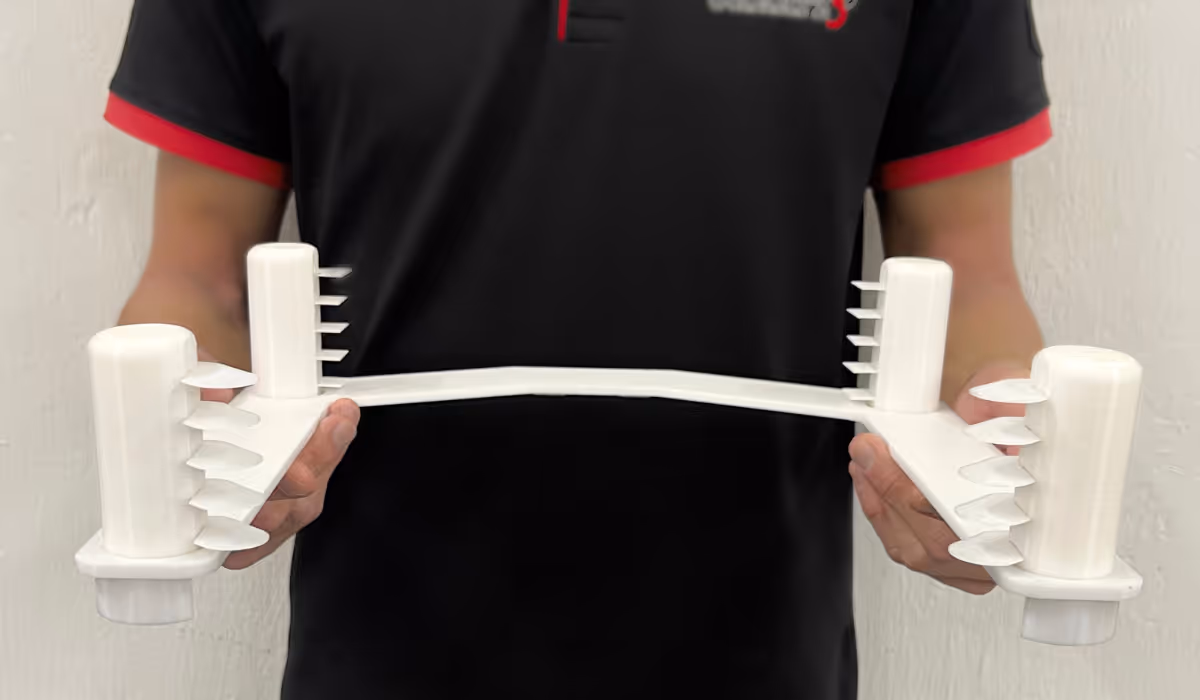 Person holding a white plastic 3D-printed teaching jig with four vertical posts and multiple horizontal fins.