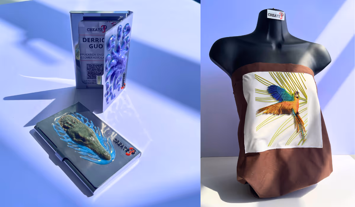 Two artistic name badges on a blue surface: left shows a hand and footprint design, right features a mannequin draped with fabric displaying a colorful bird embroidery.