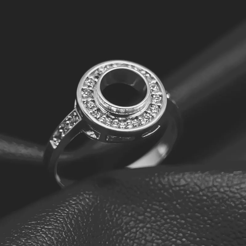 Silver ring with a circular hollow center surrounded by small diamonds on a black textured surface.