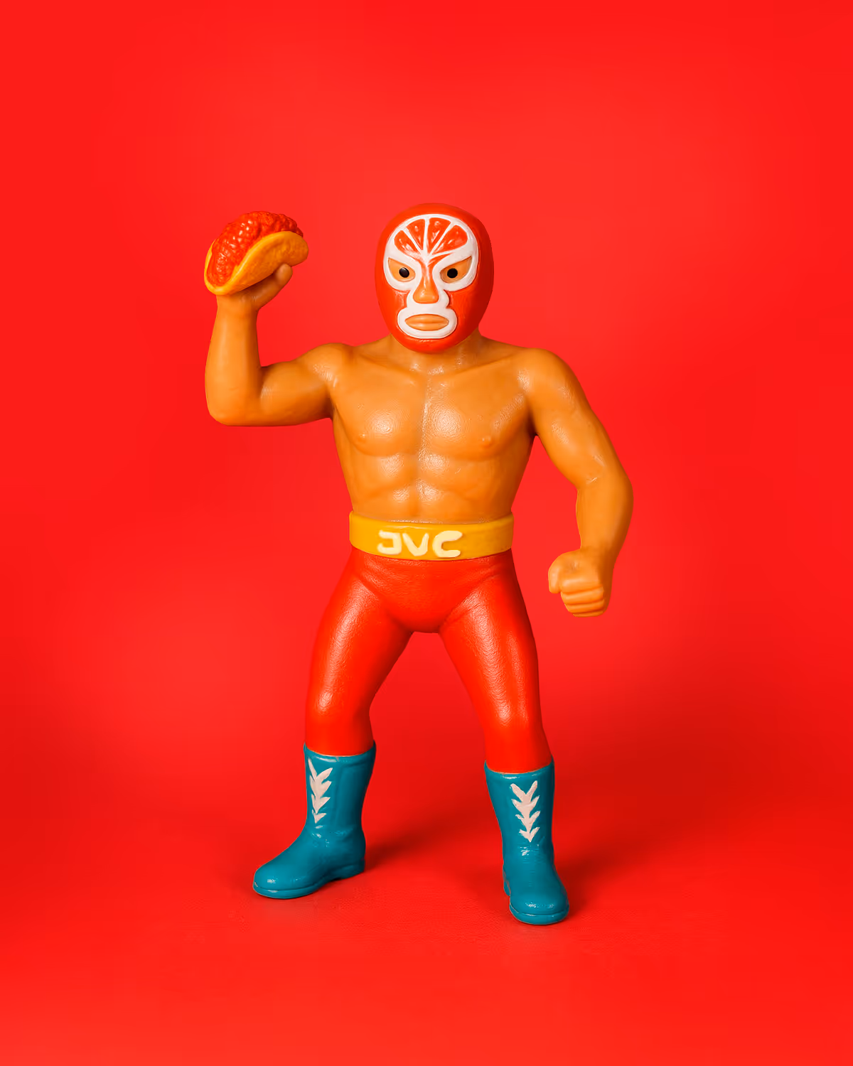 Plastic action figure of Yoyoman, a masked Mexican luchador holding a taco, wearing red tights and turquoise boots, posed against a red background — Tacos Yoyo brand mascot.