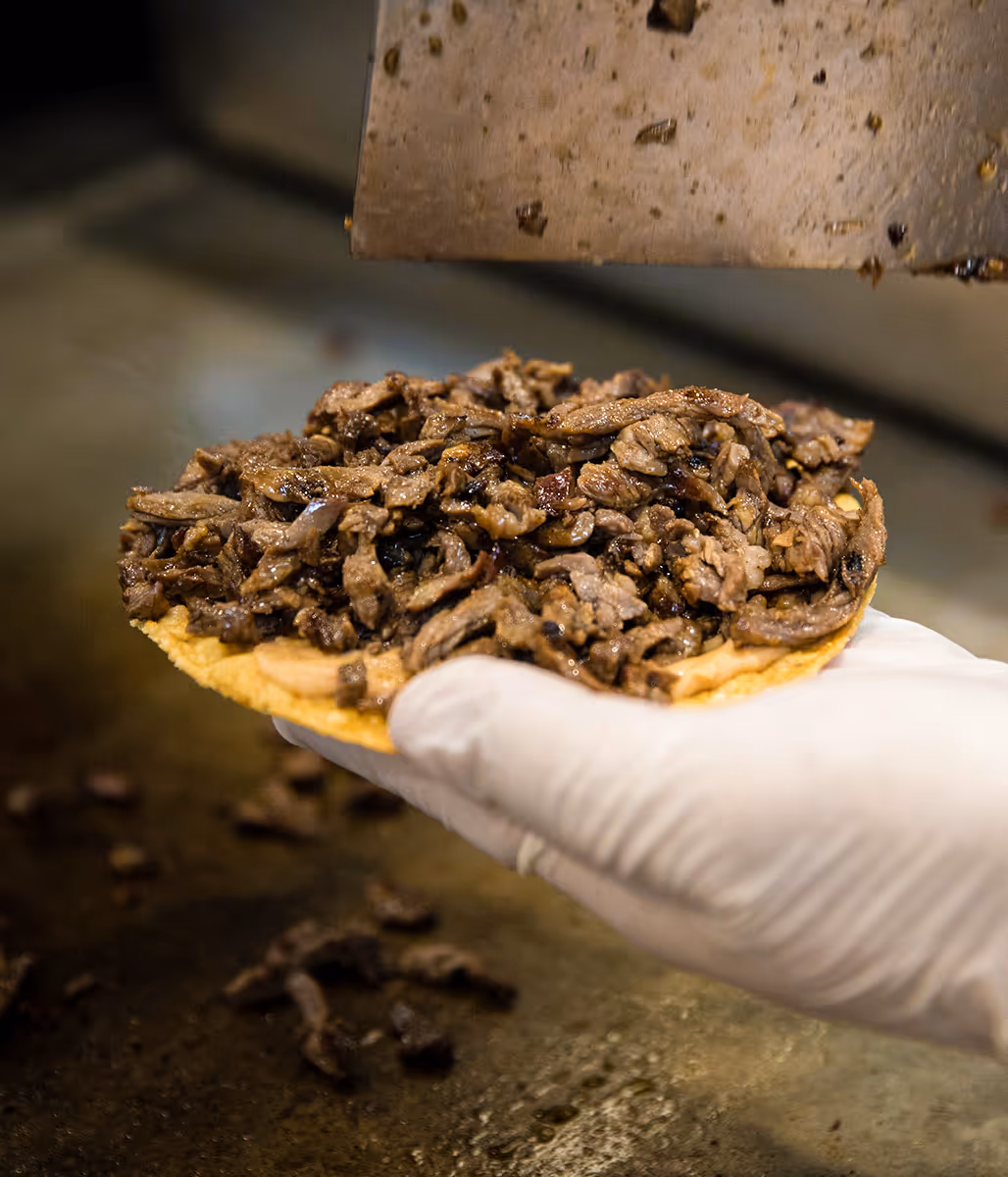 Close-up of a taco being prepared with grilled beef on a corn tortilla at Tacos Yoyo, a Mexican taquería in Miami.