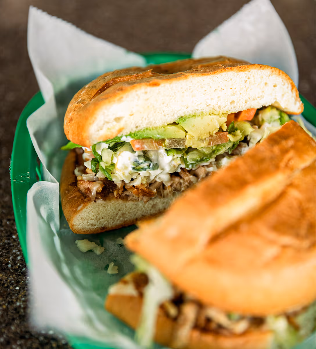 Mexican torta sandwich filled with shredded meat, avocado, lettuce, tomato, and crema, served at Tacos Yoyo in Miami.