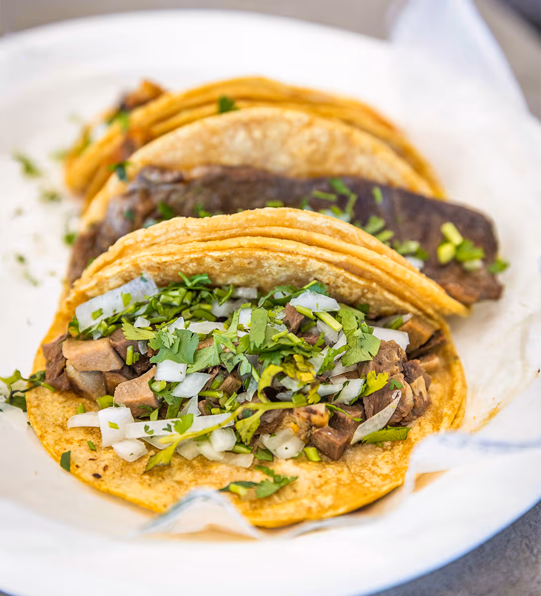 Three Mexican street tacos with grilled beef, onions, and fresh cilantro on corn tortillas, served at Tacos Yoyo in Miami.