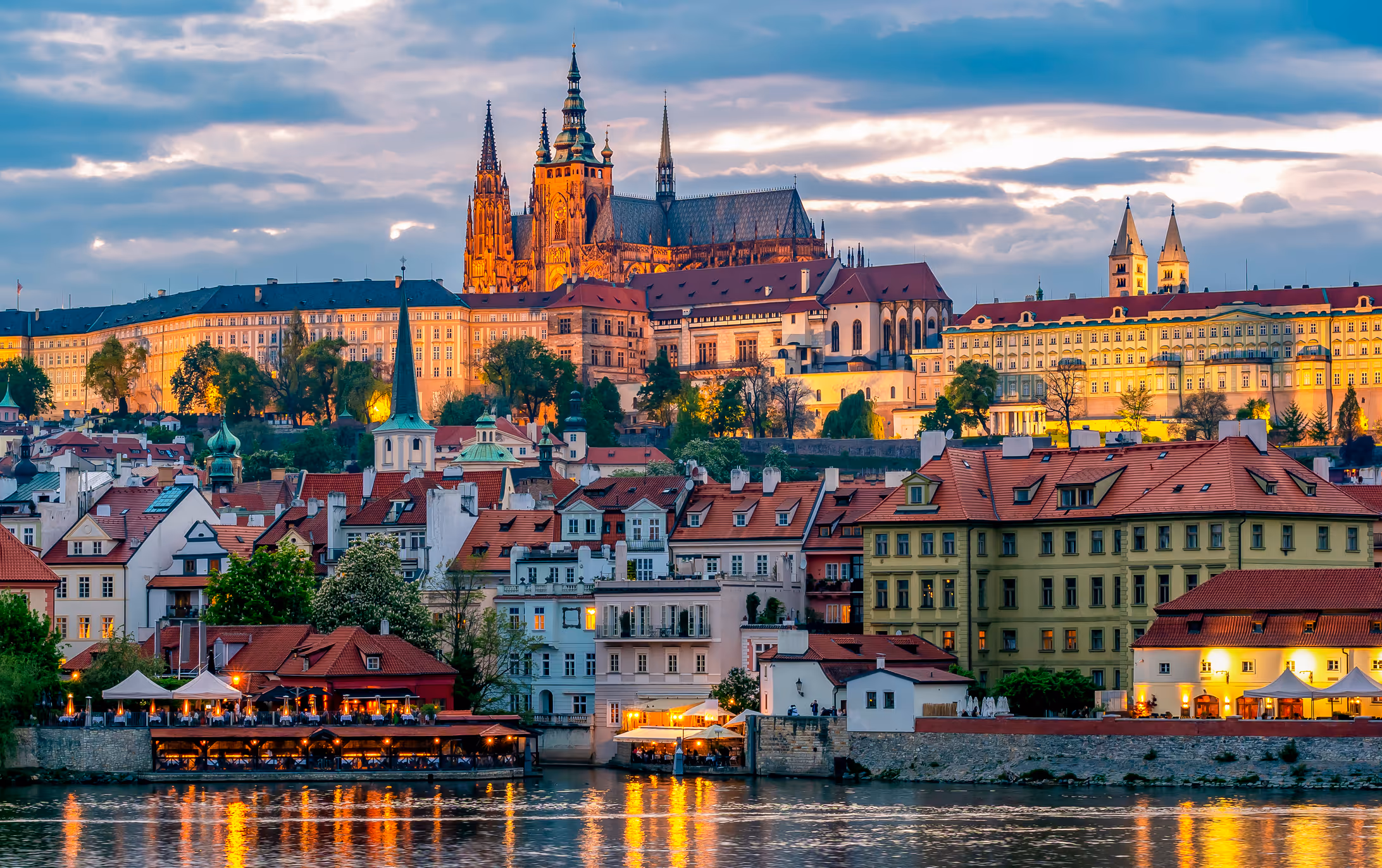 Panoramic view of Prague Castle illuminated at sunset with traditional houses along the Vltava River in Prague, Czech Republic