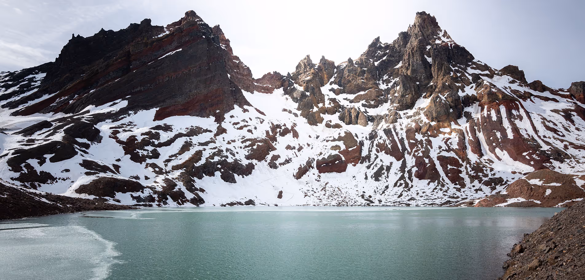 a body of water with snow on the side of a mountain
