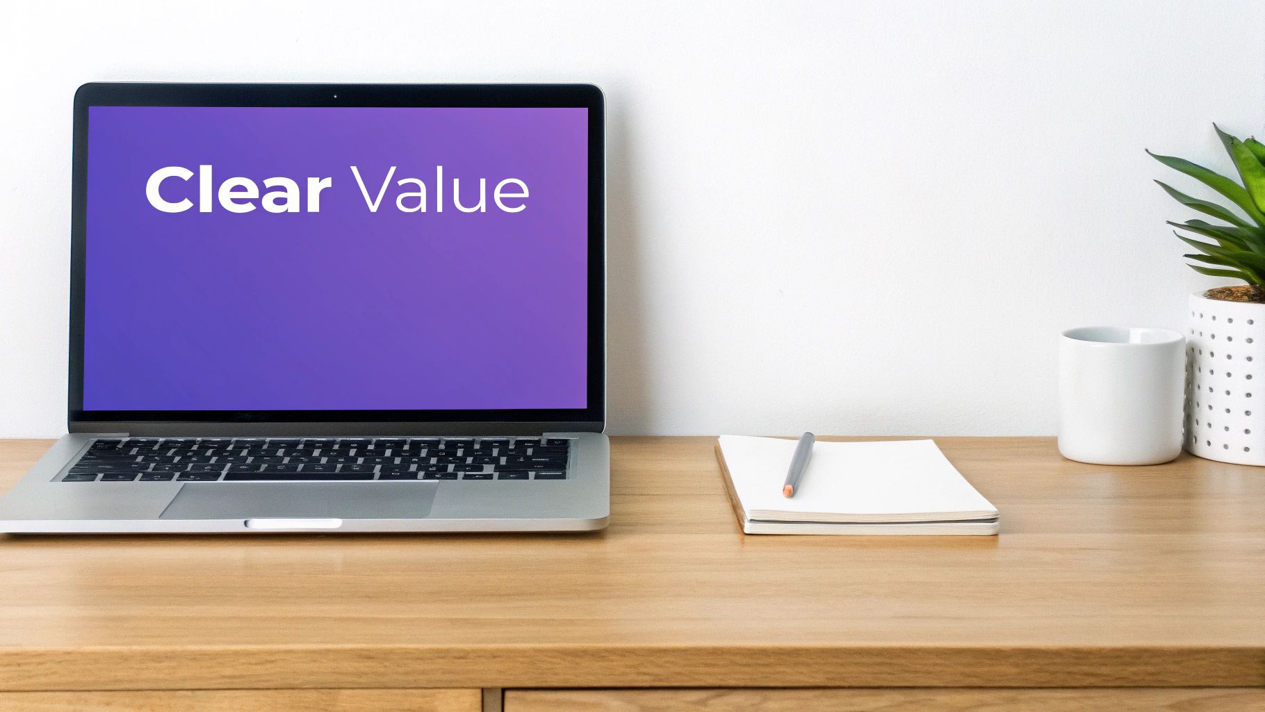 A clean desk setup with a laptop displaying 'Clear Value' on a purple screen, a notebook, and a plant.