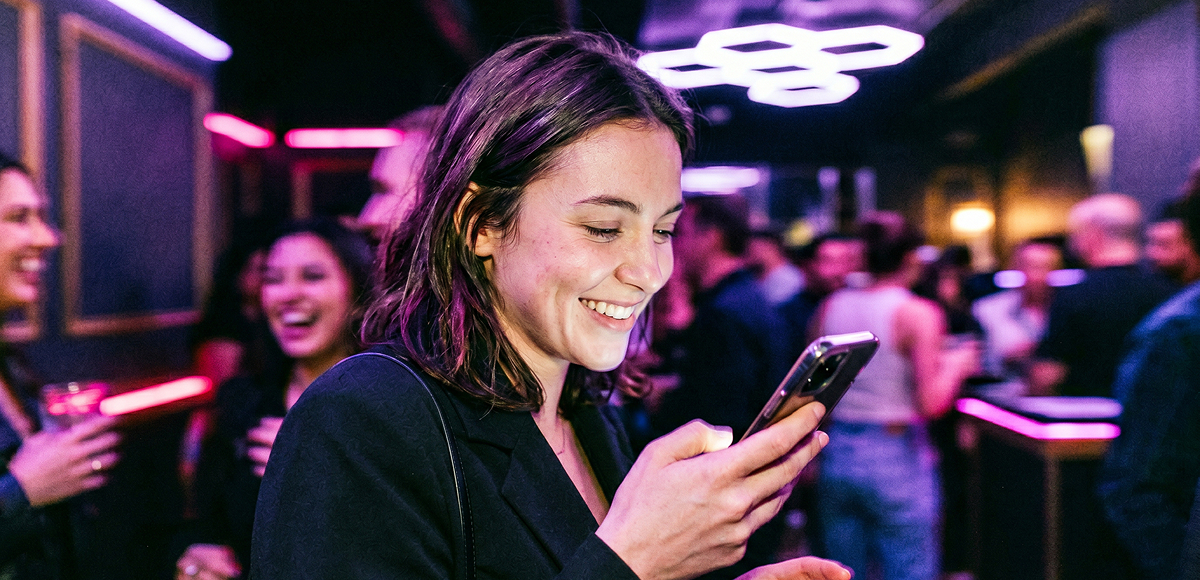 Young woman smiling at phone with friends in background at Grid City VR entertainment venue in Westminster CO