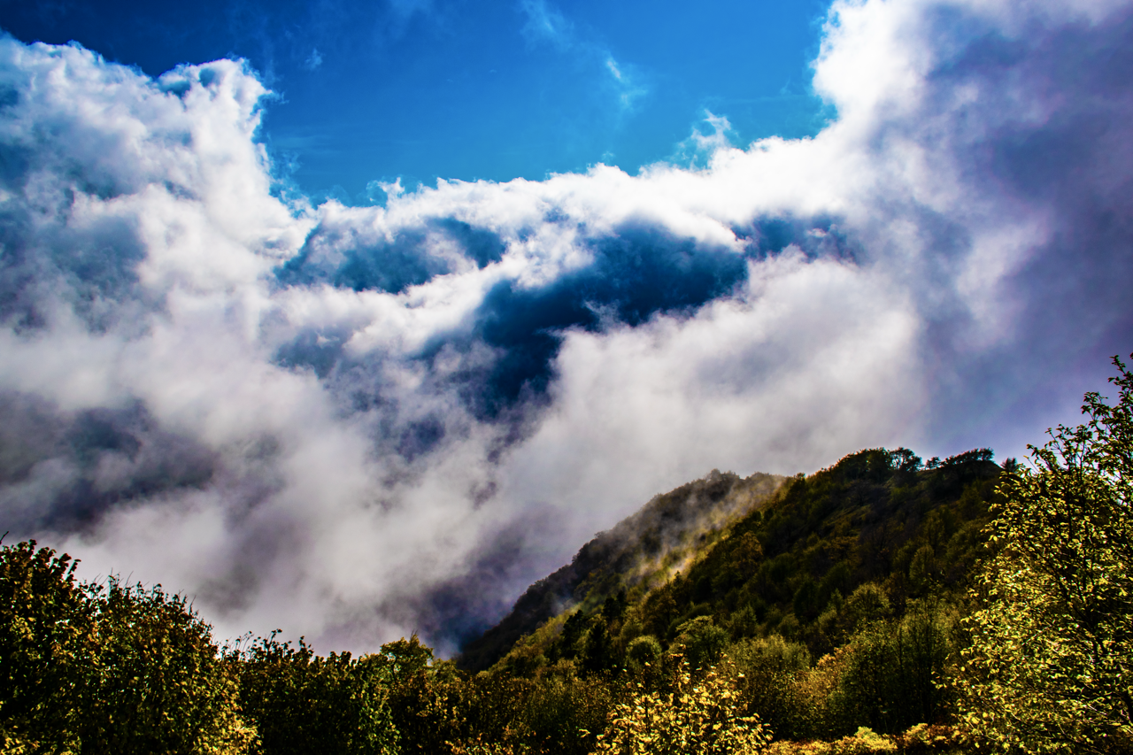 Forest-covered hills under dramatic clouds with blue sky peeking through.
