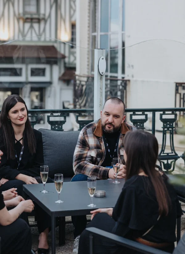 People sitting around an outdoor table, chatting and drinking from champagne glasses.