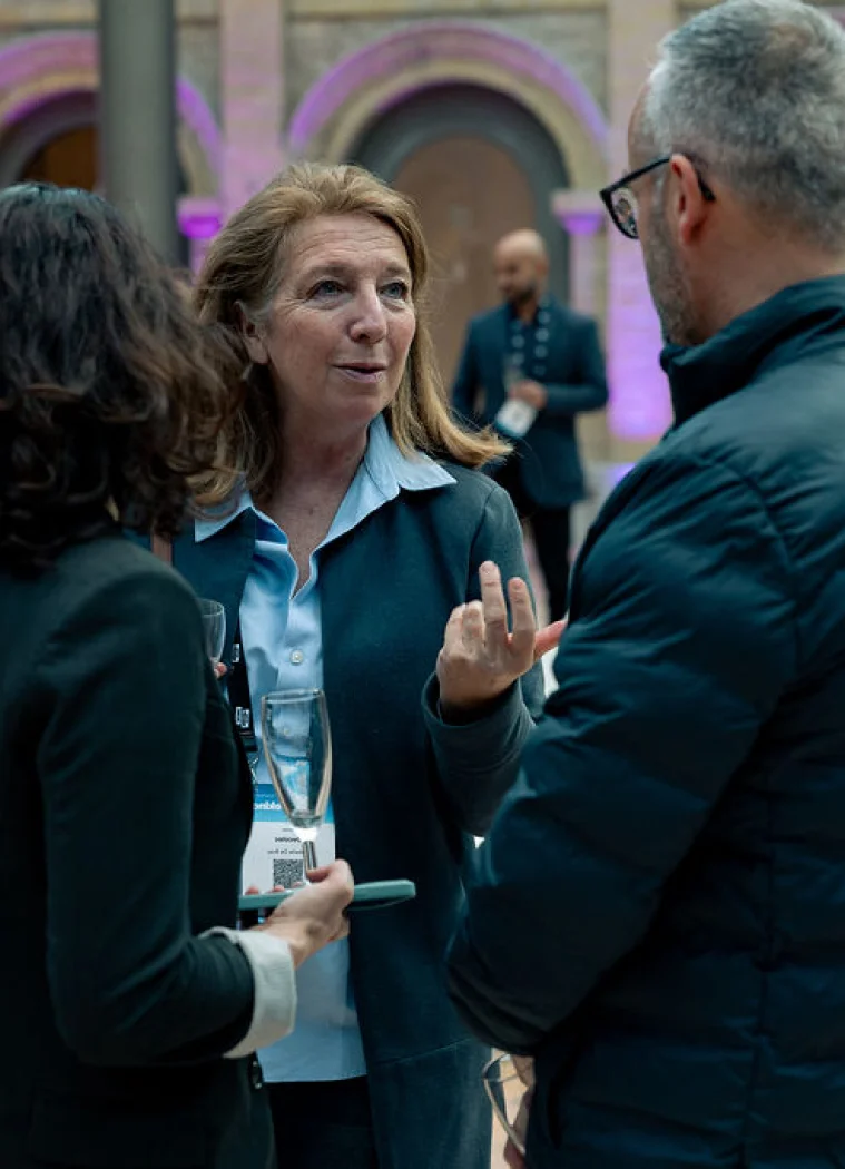 A woman gestures while talking with two people holding drinks.