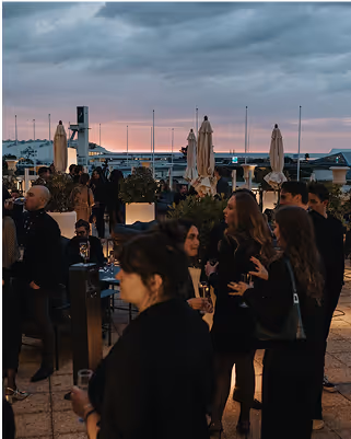 People gathered at a rooftop event during sunset, socializing and enjoying drinks.