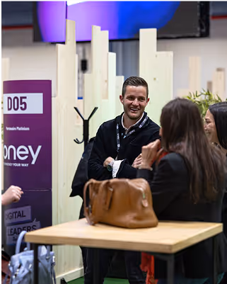A man and three women chat and laugh around a table at an indoor event.