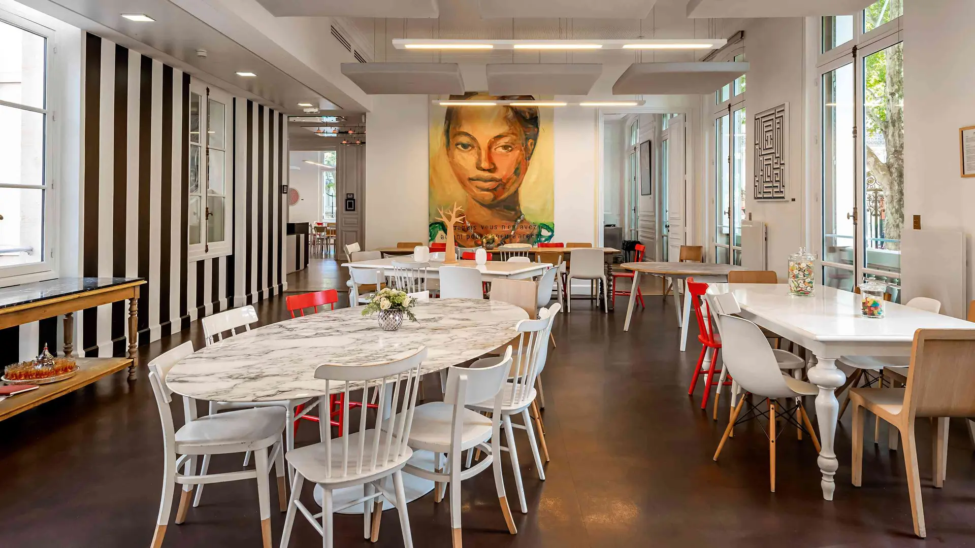 Dining area with several tables and chairs, featuring a large portrait on the wall.