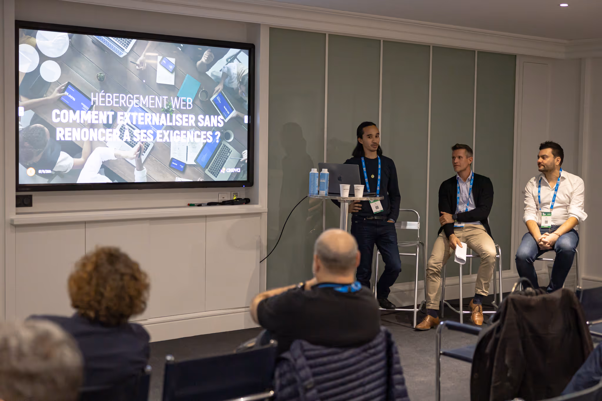 Three people in a meeting room discuss a presentation displayed on a large screen.