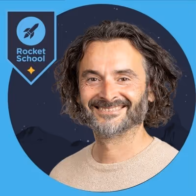 Smiling man with curly hair in a beige sweater, beside a "Rocket School" logo.