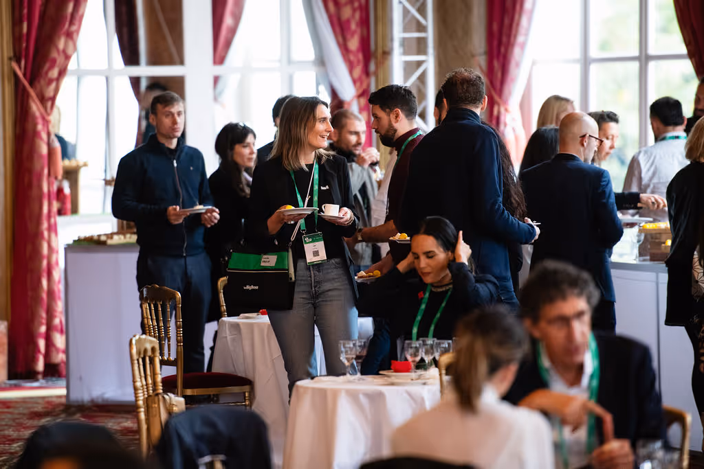 People mingling and eating at a conference event, some standing and others sitting at tables.