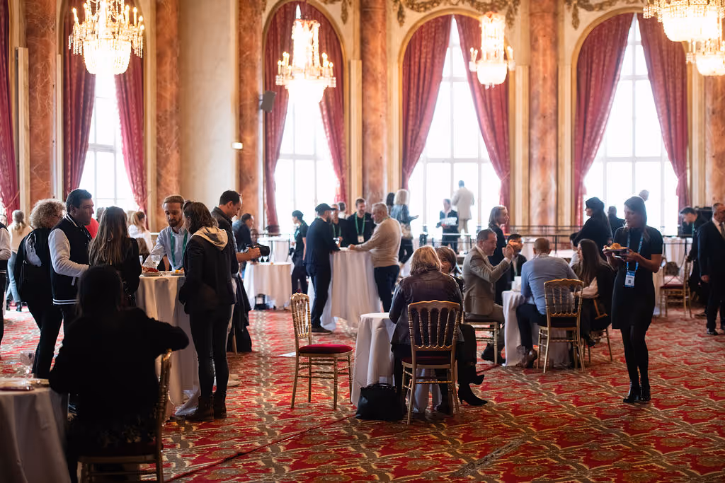 People standing and sitting at small tables, talking and networking in a large, elegant room.