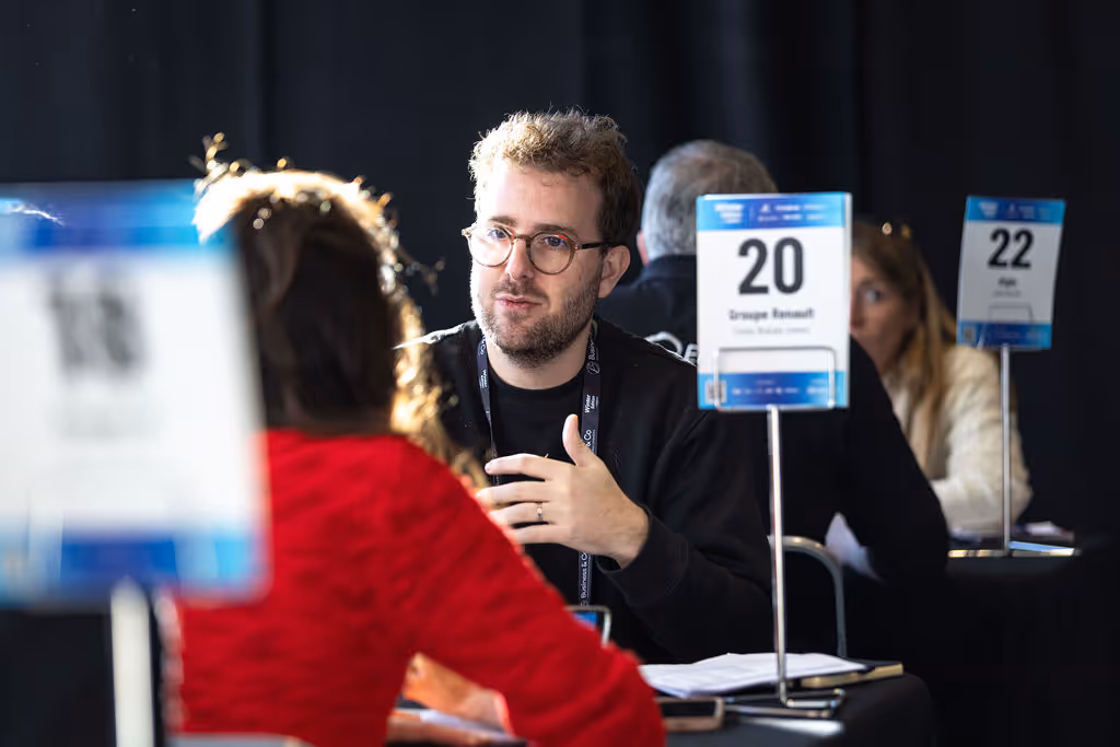 A man is talking to a woman across a table, with numbered signs in the background.