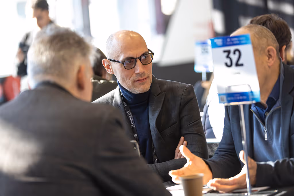 Three men having a conversation at a table with a number 32 sign.