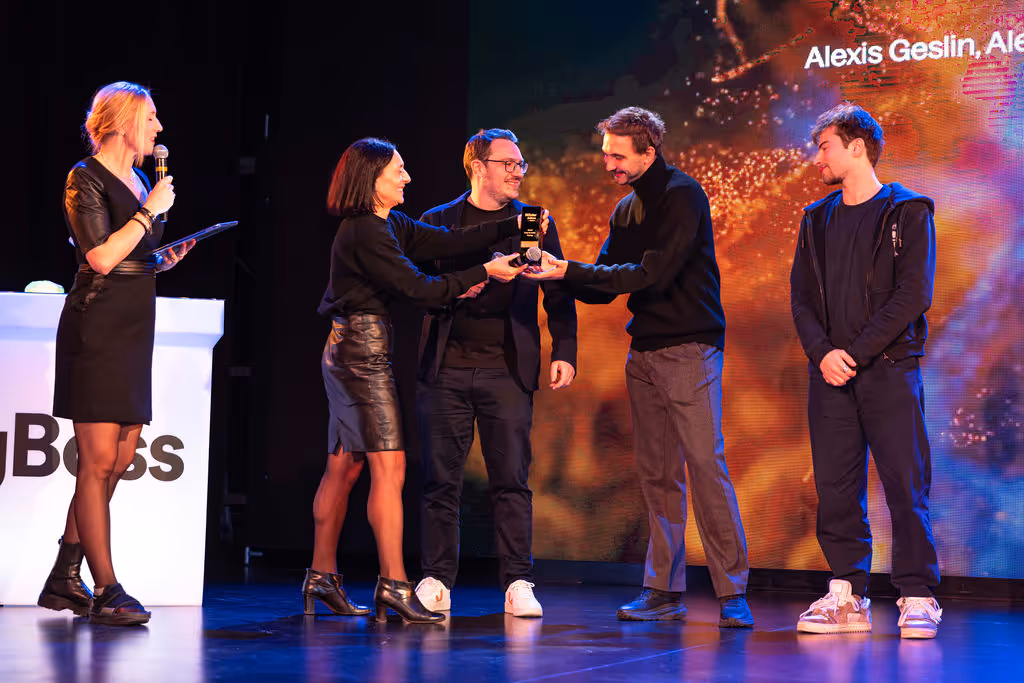 Four people stand on stage, presenting an award to a man, while a woman speaks into a microphone.