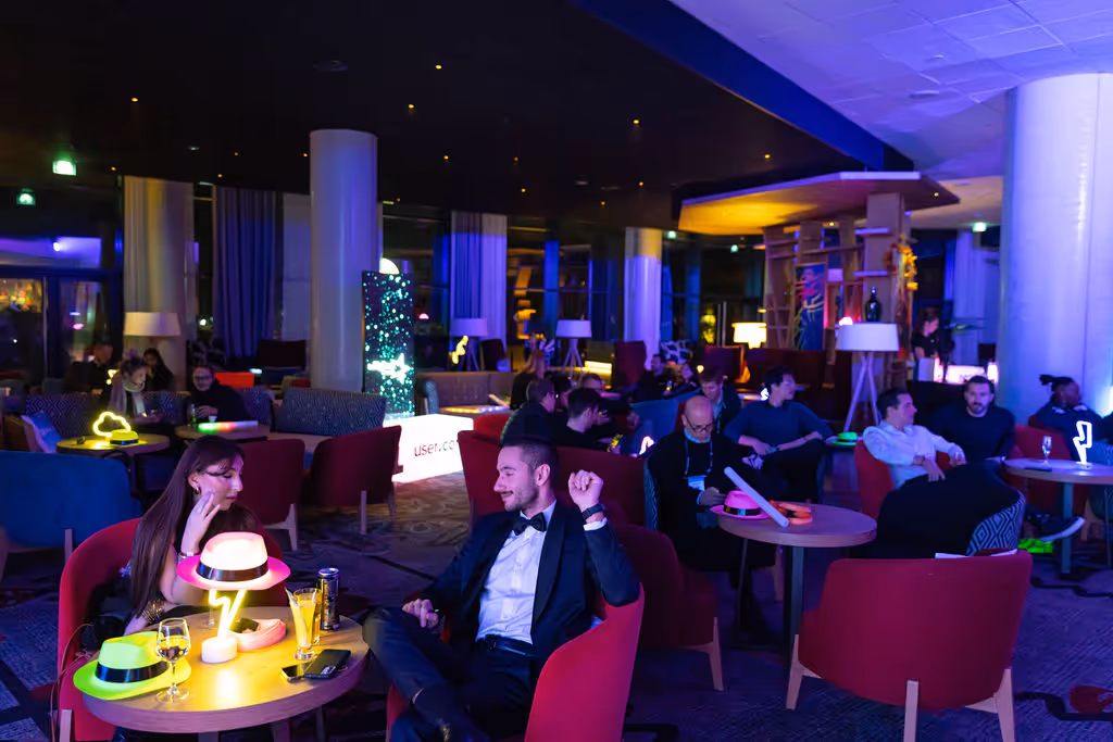 People sitting in a dimly lit lounge, enjoying drinks and conversations around small tables.