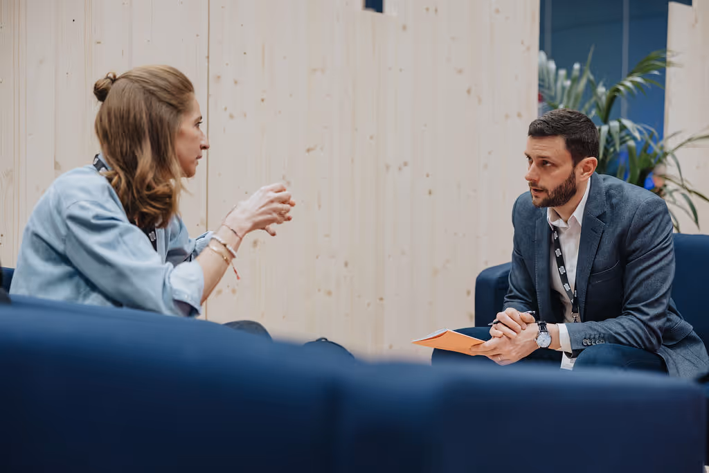 Two people sitting on blue sofas, engaged in a focused conversation.