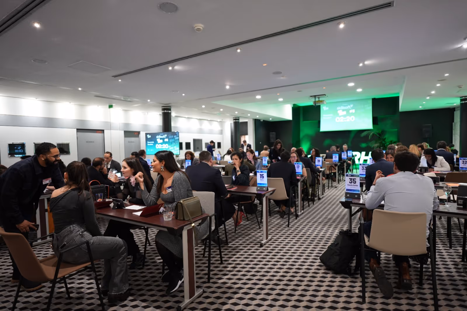 People seated at tables in a conference room, engaged in discussions or meetings.