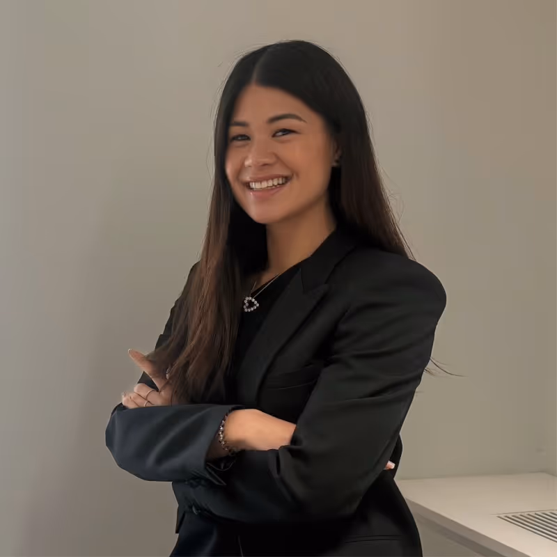 A person in a black blazer smiles with arms crossed, standing against a plain background.