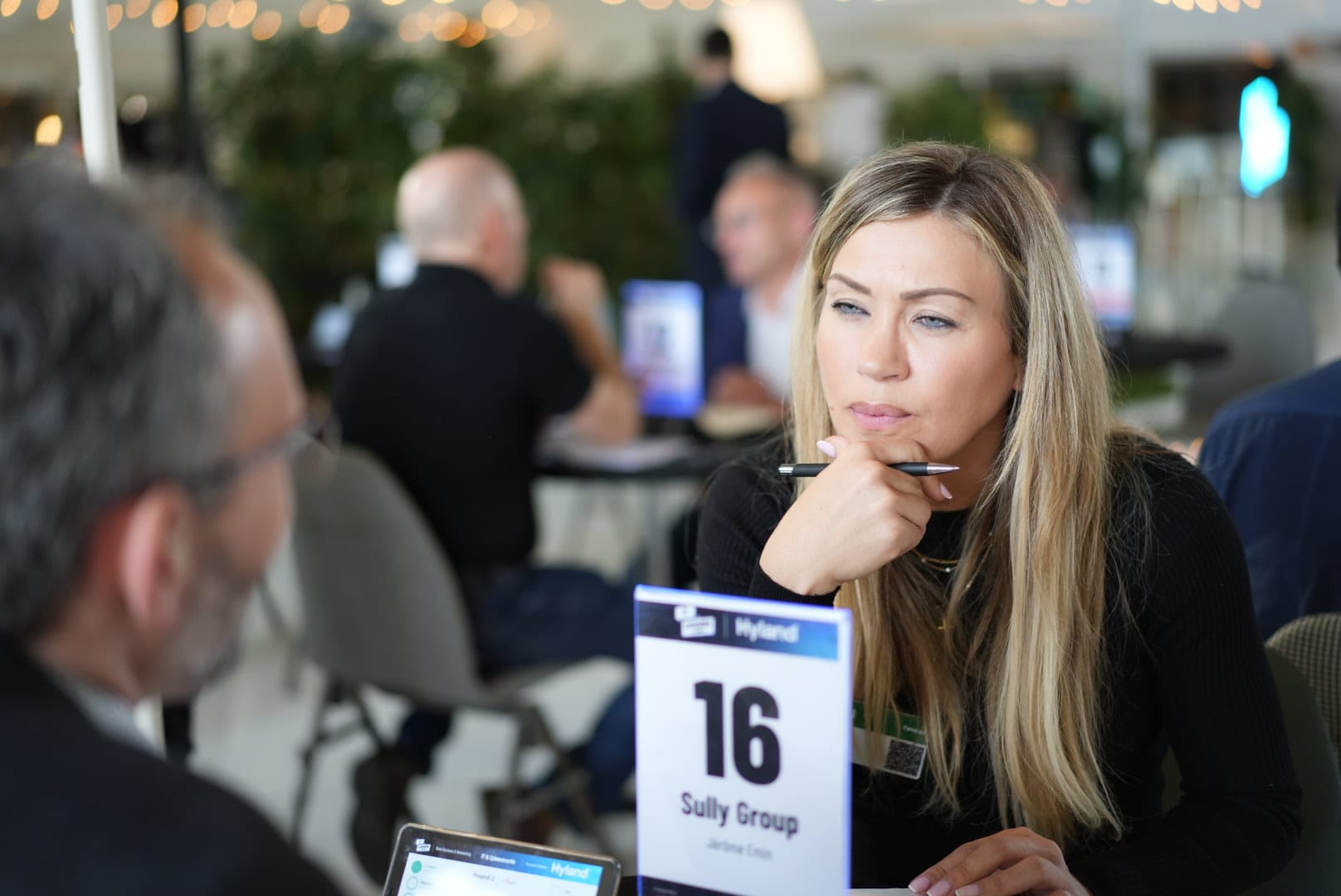 Woman attentively listens during a business meeting, holding a pen with a conference table number in view.